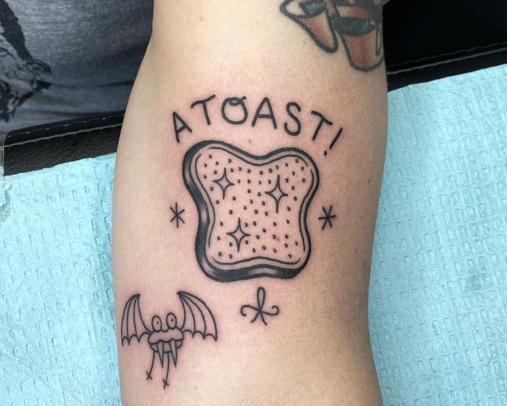 tattoo with a toast, little monster and the inscription "atqast"