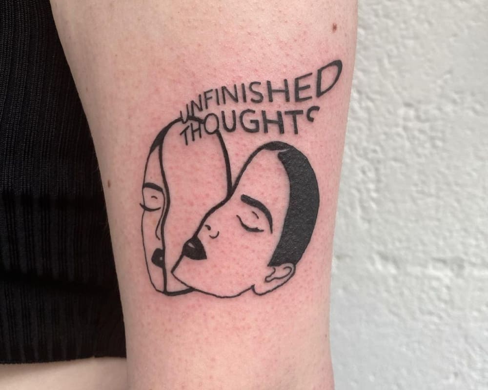 A tattoo in the form of a head divided in half and the inscription unfinished thought
