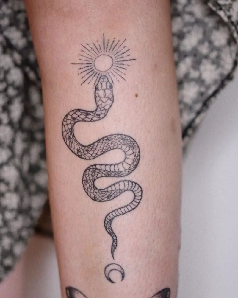 A tattoo of a snake with a crescent moon on its tail and the sun on its head