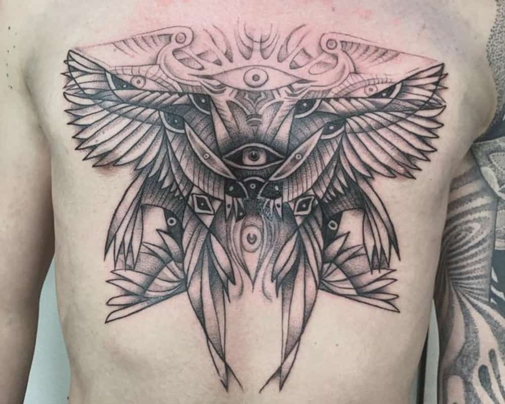 Egyptian-inspired tattoo of wings with eyes on chest