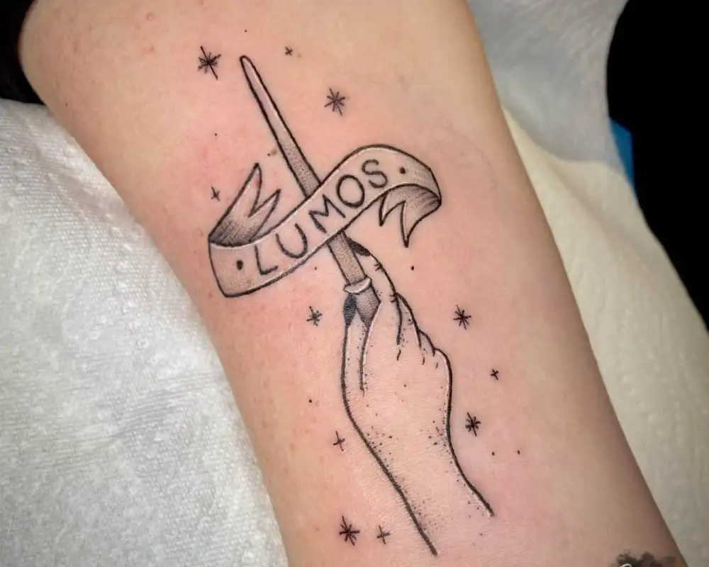 Tattoo of a hand with a magic wand and the phrase Lumos