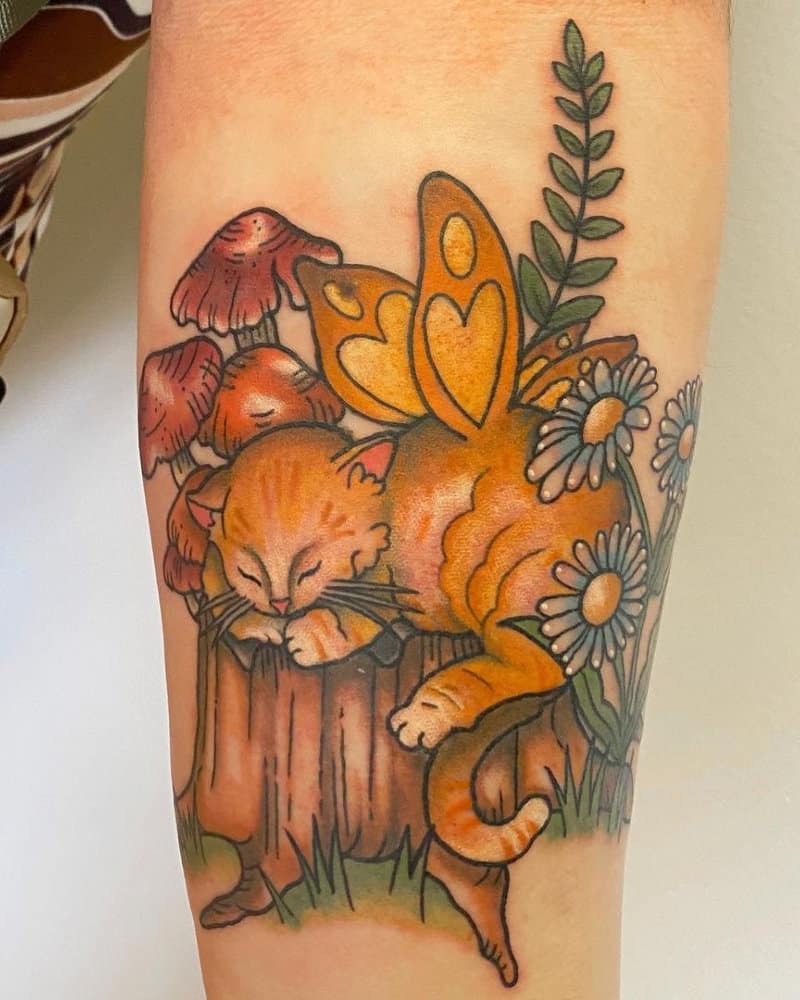 Tattoo of a kitten sleeping on a stump with wings, with flowers and mushrooms around it