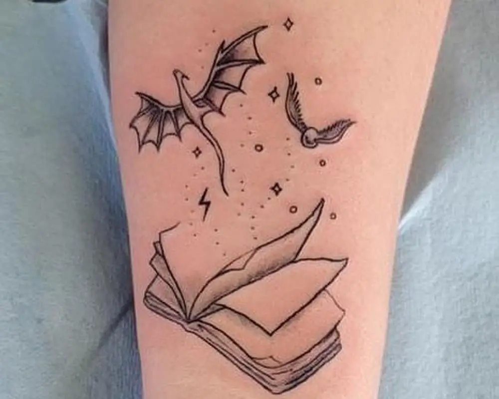 Tattoo of a sign book with a dragon and a golden snitch flying out of it