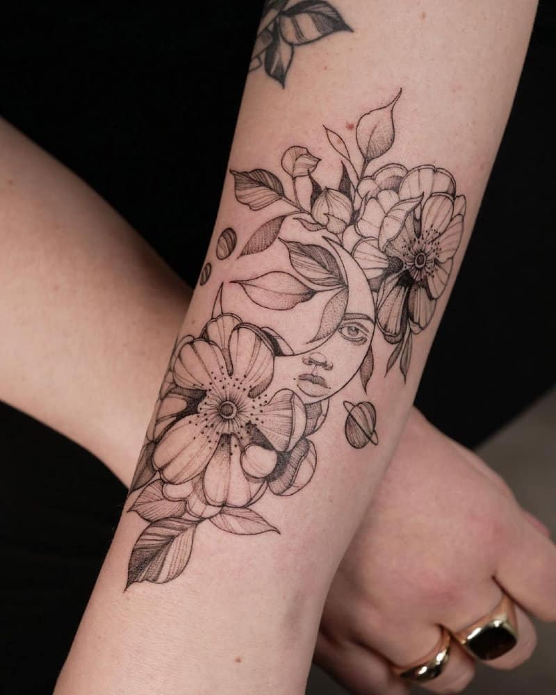 Tattoo of flowers with a girl's face on a crescent moon