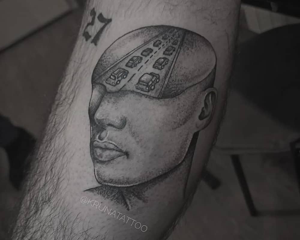  tattoo in the form of a head in the cut which shows the road with standing cars in a traffic jam
