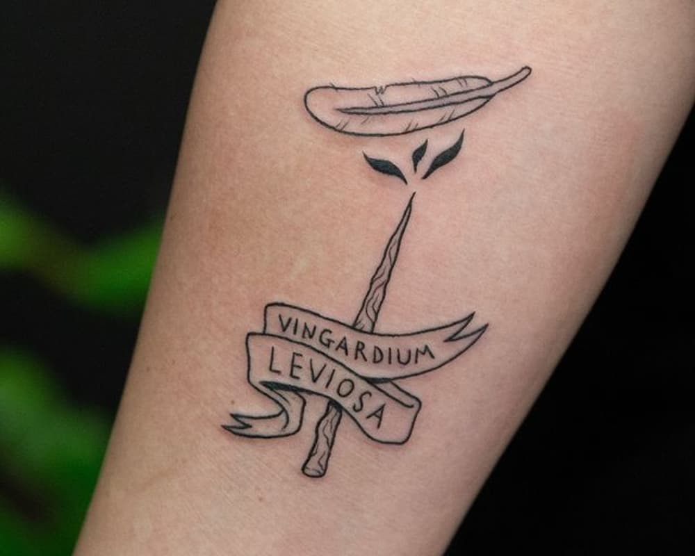 a tattoo of a magic wand and a feather with the inscription vingardium leviosa