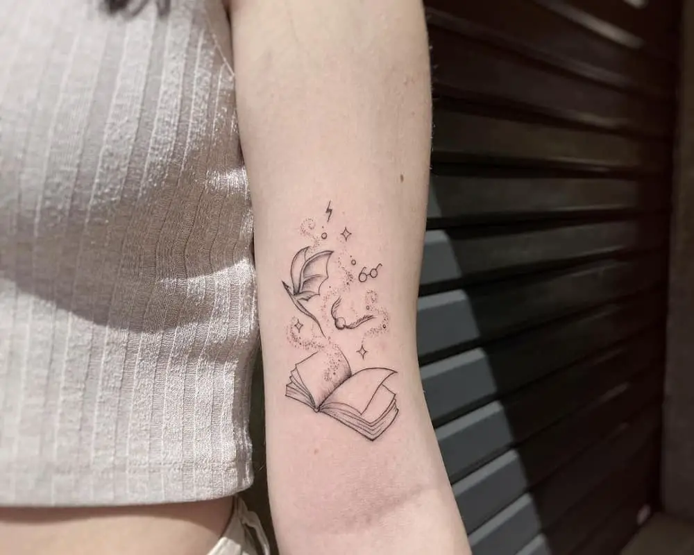a tattoo of an open book with a snitch, a dragon and glasses