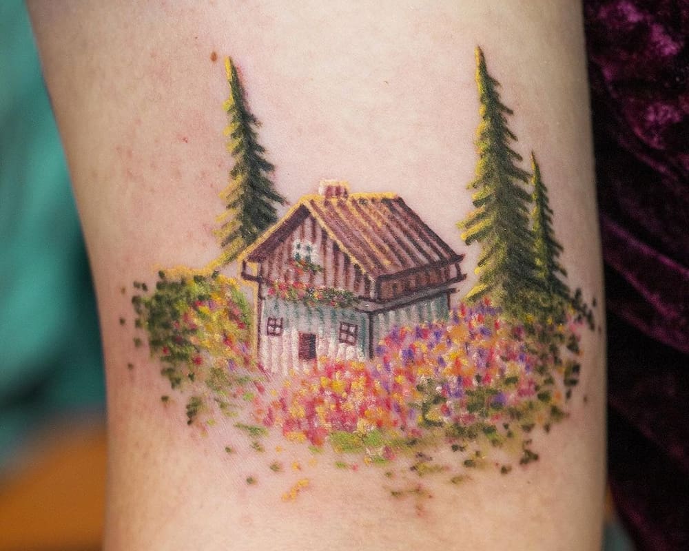 small coloured tattoo of a cottage in a meadow in the woods