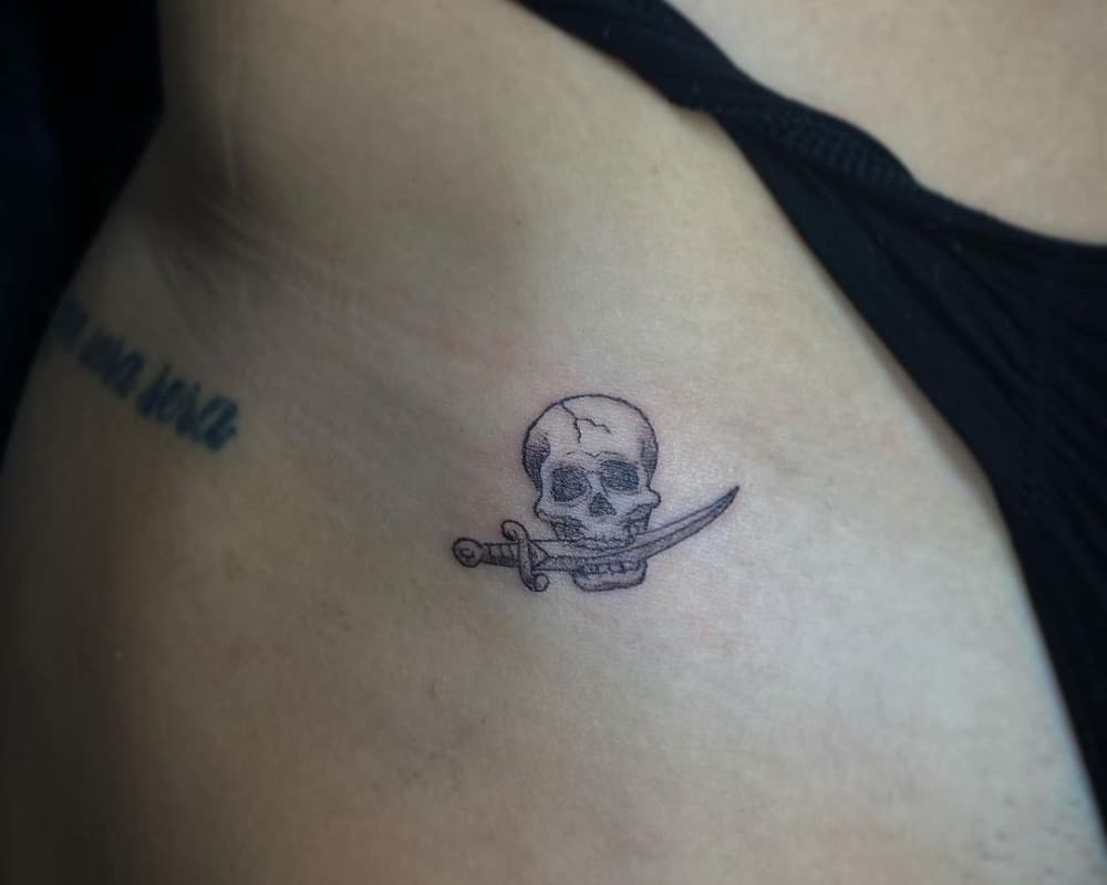 tattoo of a skull with a dagger in its teeth