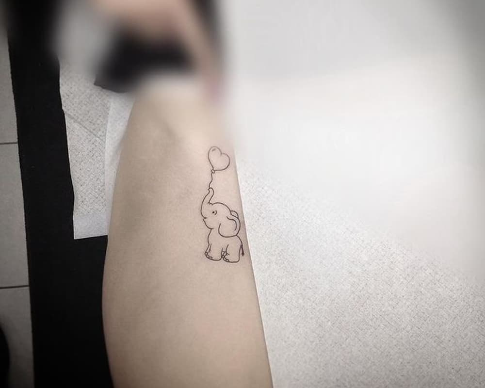 tattoo of a small elephant holding a heart-shaped ball with its trunk