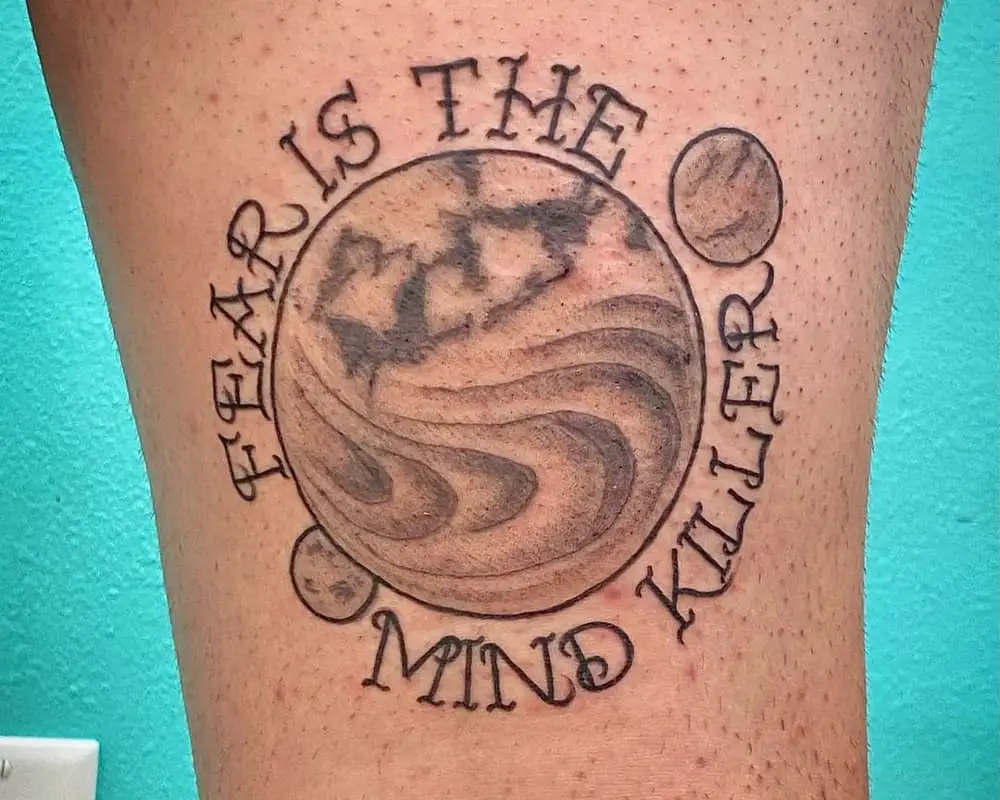 tattoo of the planet Arakis with moons and the inscription fear is the mind killer