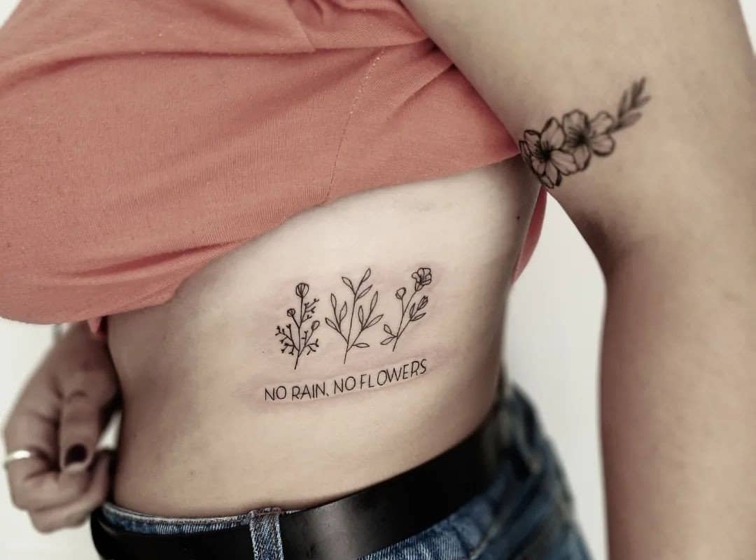 tattoo of three flowers and the inscription "no rain no flowers"